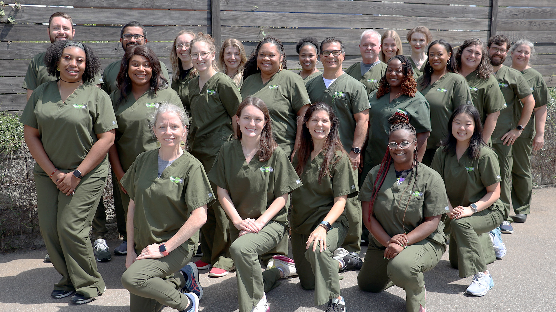 A group of men and women smiling in green clinical scrubs