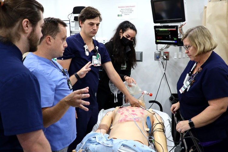 A group of medical professionals wearing medical scrubs standing around a simulation manikin during a clinical simulation