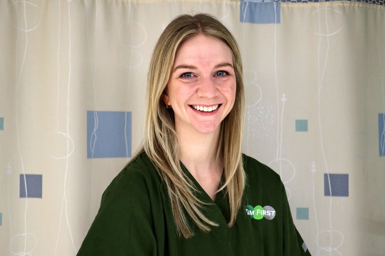A smiling woman wearing olive green medical scrubs