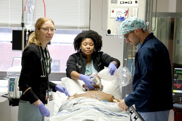 Two female nurses and one male nurse practicing ventilating a simulation manikin