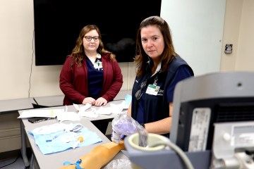 A woman in medical scrubs demonstrating intravenous line insertion to another woman in medical scrubs