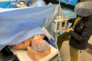 A woman wearing medical scrubs and a UAB Medicine jacket sets up a simulation manikin in a simulated operating room.