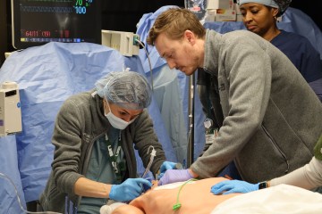 Three health-care team members simulating a procedure on a simulator manikin