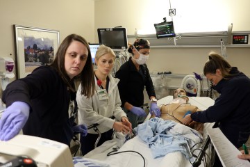 Four female nurses simulate a medical procedure on a simulation manikin.