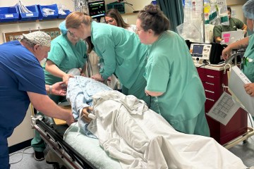 One male and two female nurses in blue and green scrubs, respectively, simulating a cardiac arrest response on a simulation manikin