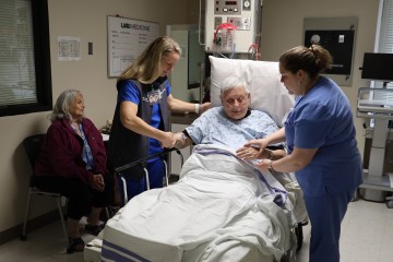 Two women in scrubs participating in an age-friendly care simulation with one female standardized patient and one male standardized patient