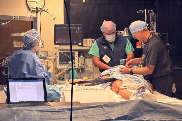 A woman and two men, each in medical scrubs, participating in an anesthesiology simulation