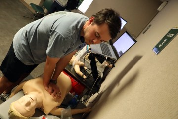 A caucasian male practicing CPR on a health-care simulation manikin