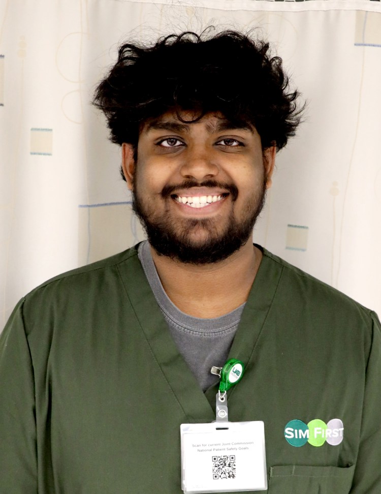 A dark-skinned man in olive green medical scrubs