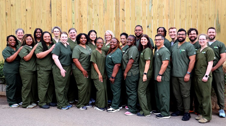 A diverse group of men and women standing together, wearing olive green medical scrubs