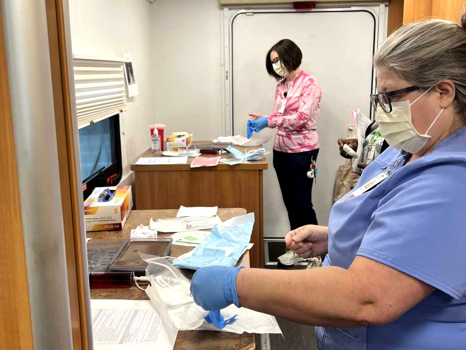 Two Caucasian women, one blue medical scrubs and the other in a pink tie-dyed shirt and black scrub pants, participating in a health-care simulation in a mobile simulation lab