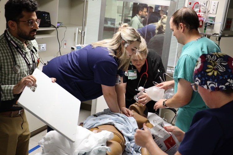 A diverse group of five medical professionals practicing code skills with a health-care simulation manikin