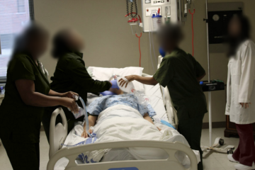 Four women in medical scrubs simulating a tracheostomy on a health-care simulation manikin