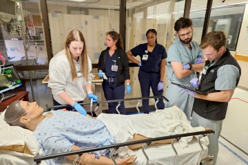 A group of nurses and medical residents participating in an emergency department simulation with a health-care simulation manikin