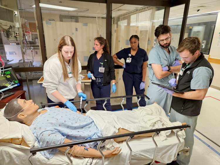 A group of nurses and medical residents participating in an emergency department simulation with a health-care simulation manikin