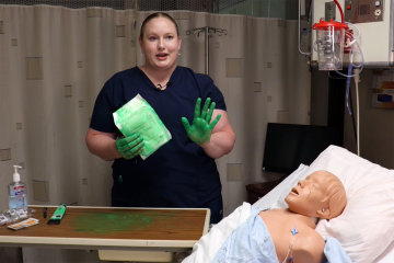 A Caucasian female nurse in navy blue scrubs with green paint on her hands to demonstrate sterile technique