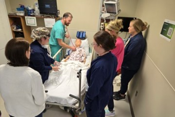 A group of medical professionals participating in a pediatric health-care simulation with a pediatric health-care simulation manikin