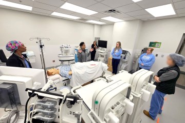 Four women in medical scrubs participating in a health-care simulation in a recently renovated operating room with a health-care simulation manikin