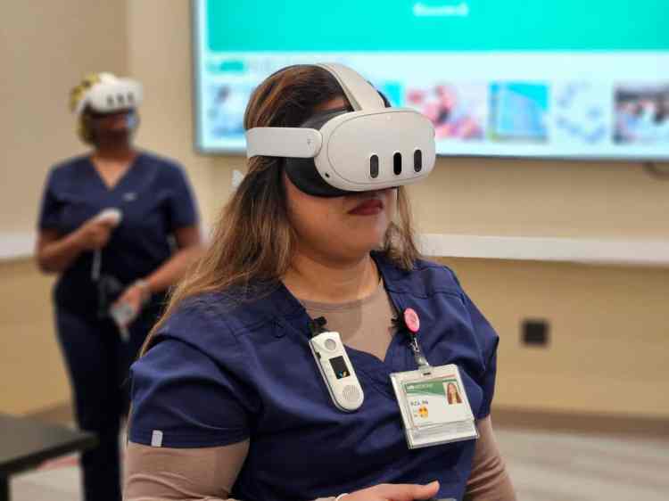 Two women in navy blue medical scrubs wearing white virtual reality headsets