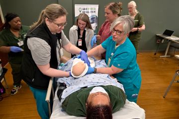 Four nurses participating in a obstetric health-care simulation featuring a standardized patient, as simulation facilitators observe and assist