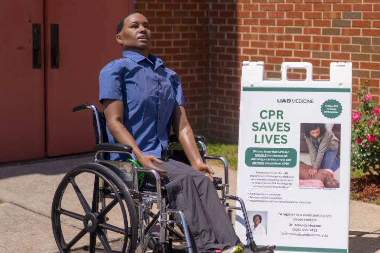 A health-care simulation manikin sitting in a wheelchair next to a sign advertising CPR training