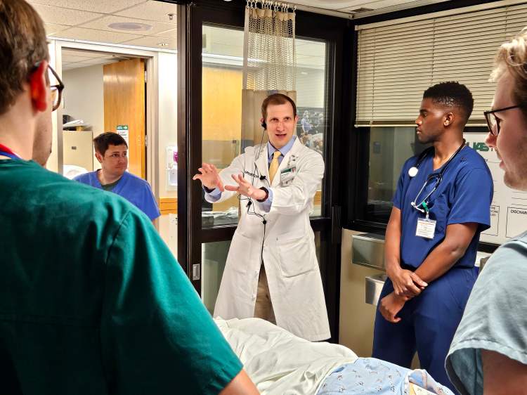 A physician in a white lab coat instructing medical residents in various colored medical scrubs