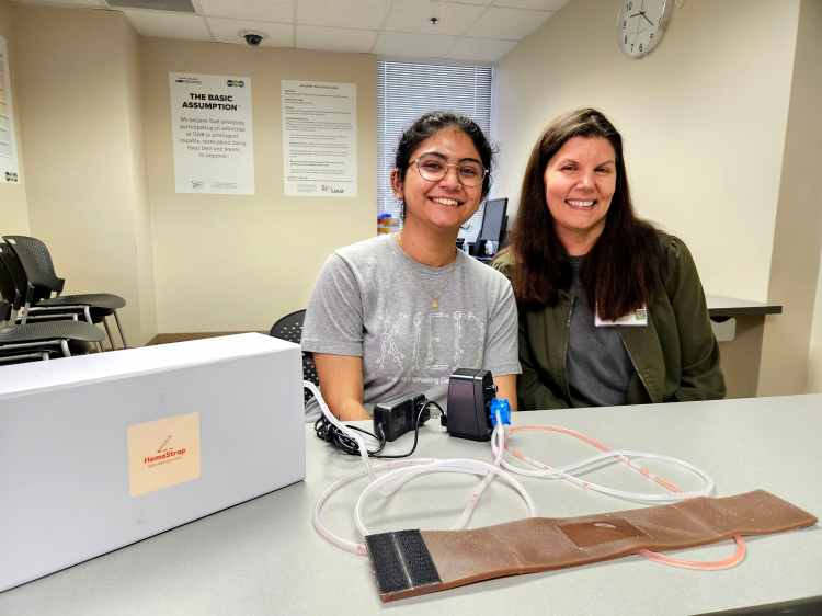 A female graduate student and female health-care simulation coordinator sitting behind a table topped with a new simulation trainer