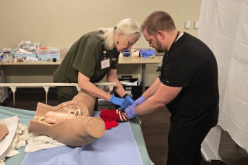 A woman in olive green medical scrubs guiding a learner in black medical scrubs through an obstetrics simulation