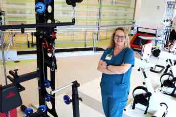 A woman in teal medical scrubs standing in a therapy gymnasium