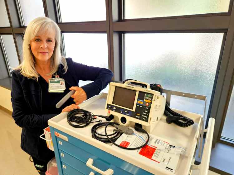A woman in navy blue medical scrubs standing next to a crash cart