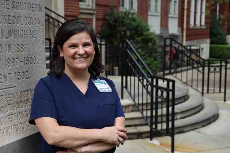 A woman in navy blue medical scrubs standing outside of a hospital