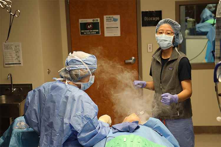 A female embedded participant portraying a surgeon and a female anesthesia resident handling a simulated airway fire with smoke rising from a health-care simulation manikin