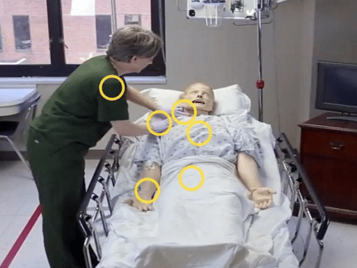 A woman in olive green medical scrubs interacting with a health-care manikin as part of a virtual health-care simulation