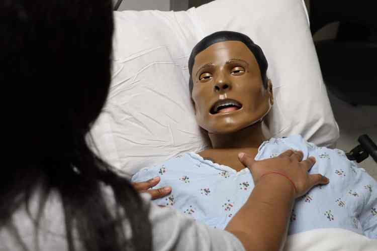 A woman with dark hair in a gray shirt jostling a health-care manikin as part of a health-care simulation