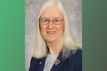 A woman in white hair wearing a navy blue blazer and striped shirt