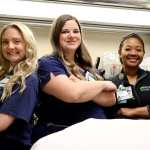 Three female nurses wearing navy blue medical scrubs