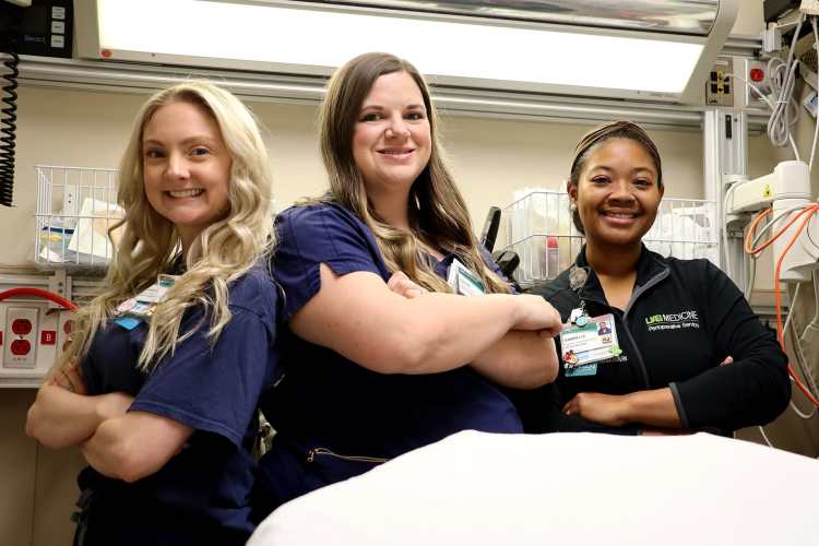 Three female nurse development specialists in navy blue medical scrubs standing together in a hospital room