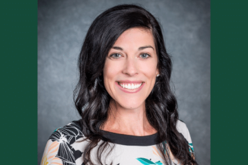 A headshot of a dark-haired woman wearing a white, black teal and orange blouse