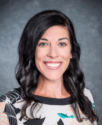 A headshot of a dark-haired woman wearing a white, black teal and orange blouse