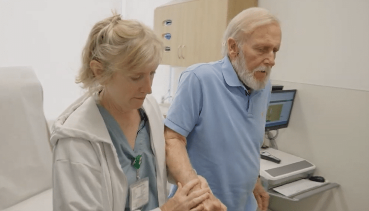 A female health-care professional helping an eldery male patient walk