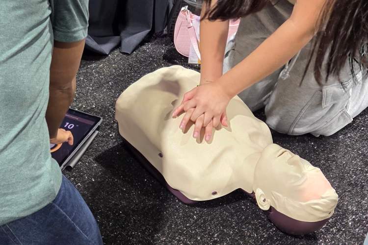 A woman performing chest compressions on a healthcare simulation manikin, as a volunteer monitors her progress