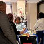 An interprofessional group of healthcare professionals surrounding a standardized patient dressed in a hospital gown portraying a disruptive patient