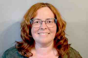 A woman with red hair and glasses wearing a dark blouse