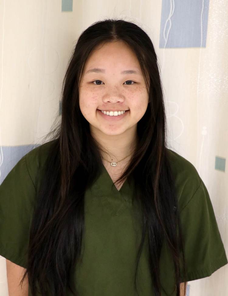 A dark-haired young woman in olive green medical scrubs